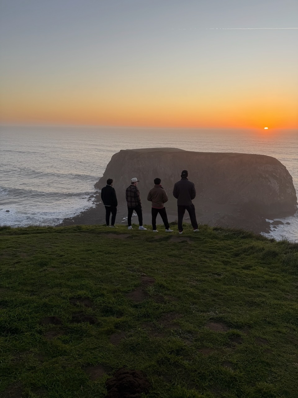 Four friends watching sunset over coastal rock formation